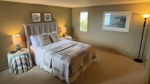 Ein Schlafzimmer mit einem Bett, zwei Nachttischen, einer Lampe, einem Fenster und einem gerahmten Bild an der Wand.