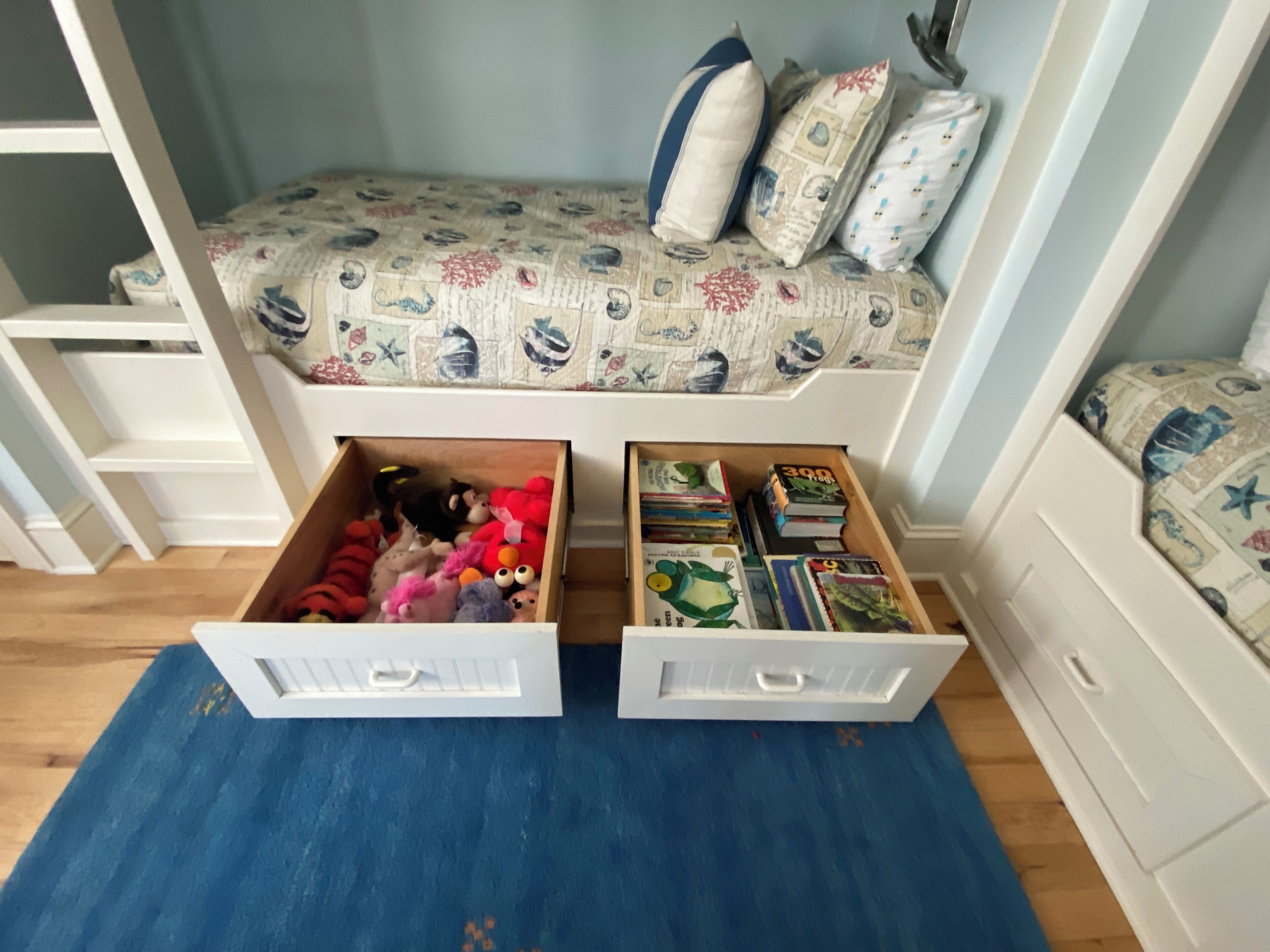 A child's bedroom with a bed, two open storage drawers, and a blue rug.