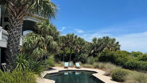 A pool area with two lounge chairs and a small table, surrounded by lush greenery and a building with a balcony. - Memory Making Oceanfront, 5BR/5BA Mansion, Pool (Isle of Palms)