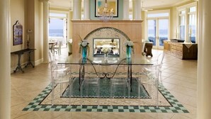 A spacious dining area with a glass table and chairs, a chandelier, and a view of the ocean. - Memory Making Oceanfront, 5BR/5BA Mansion, Pool (Isle of Palms)