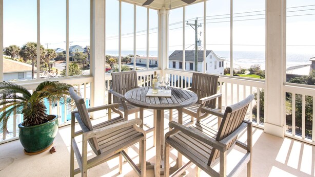 Un patio cubierto con una mesa redonda y sillas, con vistas a una zona residencial y al océano.