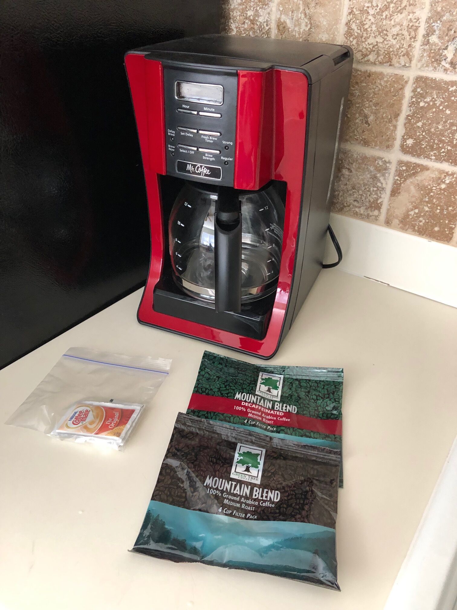 A red and black coffee maker on a kitchen counter with two packets of Mountain Blend coffee.