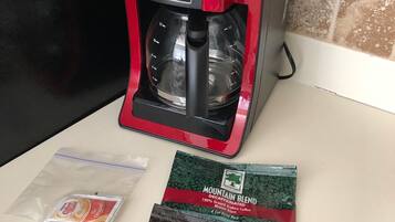 A red and black coffee maker on a kitchen counter with two packets of Mountain Blend coffee.