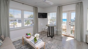 A spacious living room with a ceiling fan, a flat-screen TV, a dining area with a round table and chairs, and large windows with curtains. - Gulf Views!/corner unit/deeded beach access/pickleball courts (Santa Rosa Beach)