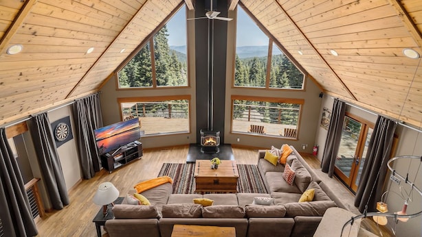 A cozy loft-style living room with a large window, a fireplace, and a modern ceiling fan. - Pet-Friendly Mountain View Retreat | Near Lake & Trails | Rec Center Access (Truckee)