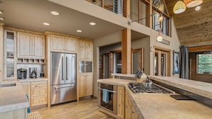 A modern kitchen with wooden cabinets, stainless steel appliances, and a large island with a gas stove. - Pet-Friendly Mountain View Retreat | Near Lake & Trails | Rec Center Access (Truckee)