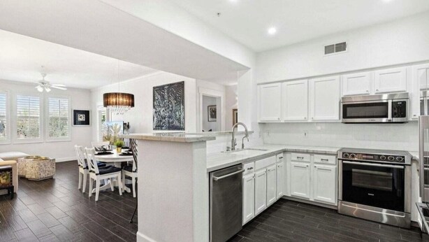 A modern kitchen with white cabinetry, a central island, stainless steel appliances, and a dining area with a white table and chairs. - WELL DRESSED GRAYHAWK CONDO! QUIET OPEN BRIGHT...Close to all the good stuff! (Scottsdale)