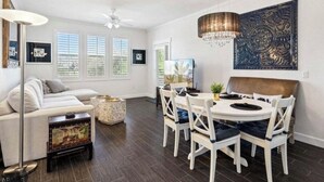 A spacious living room with a white sofa, a dining table with four chairs, a chandelier, and a large decorative wall piece. - WELL DRESSED GRAYHAWK CONDO! QUIET OPEN BRIGHT...Close to all the good stuff! (Scottsdale)