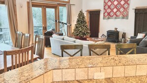 A spacious living room with a fireplace, a Christmas tree, and a large window overlooking a deck. - Custom Built by the Littlehale Family (Julian)