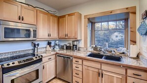 A modern kitchen with wooden cabinets, stainless steel appliances, and a large window offering a view of the outdoors. - Custom Built by the Littlehale Family (Julian)