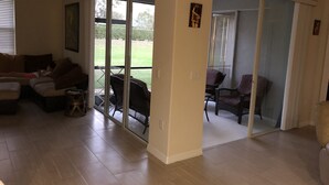A living room with a sofa, a coffee table, and a sliding glass door leading to an outdoor patio area with a table and chairs. - Golfer’s Paradise 3/2 Luxury Vacation Home (Bradenton)