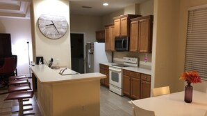 A modern kitchen with wooden cabinets, a stainless steel refrigerator, a built-in oven, and a clock on the wall. - Golfer’s Paradise 3/2 Luxury Vacation Home (Bradenton)