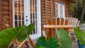 A log cabin with two large windows and a wooden deck with chairs. - Nicely Appointed Cabin in Scenic Setting. Family-friendly, Romantic Too!  (Arrington)