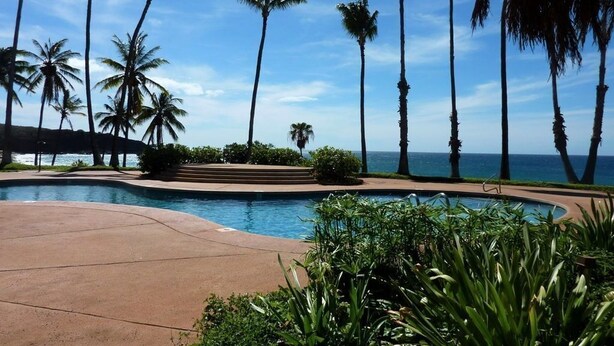 A pool area with palm trees and a view of the ocean. - Kaluako'i Resort Cottage 1A Beachfront Rental - Molokai, Hawaii (Maunaloa)