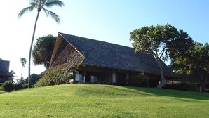 A building with a sloped roof, surrounded by a well-maintained lawn and a palm tree. - Kaluako'i Resort Cottage 1A Beachfront Rental - Molokai, Hawaii (Maunaloa)