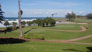 A golf course with a view of the ocean, palm trees, and a clear sky. - Kaluako'i Resort Cottage 1A Beachfront Rental - Molokai, Hawaii (Maunaloa)