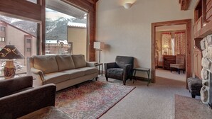 Un salon chaleureux avec un canapé, des fauteuils, un tapis à motifs et une cheminée en pierre.