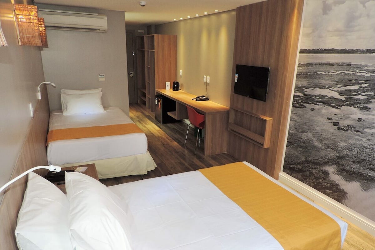 Une chambre d’hôtel avec deux lits, un bureau, une télévision et une vue sur la plage.