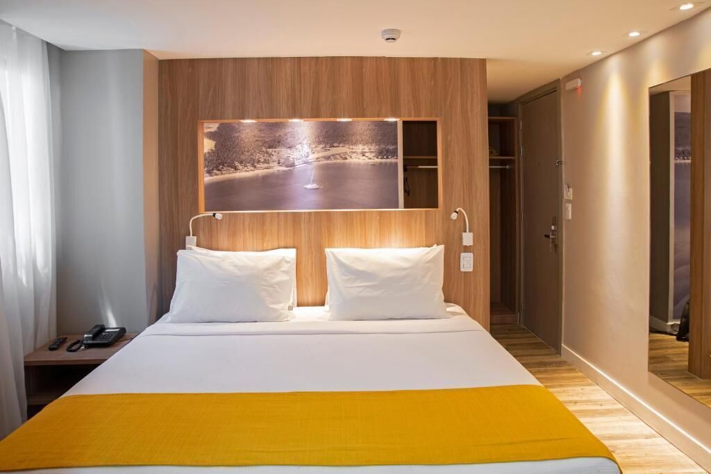 A hotel room with a bed, a nightstand, a phone, a mirror, and a picture on the wall.