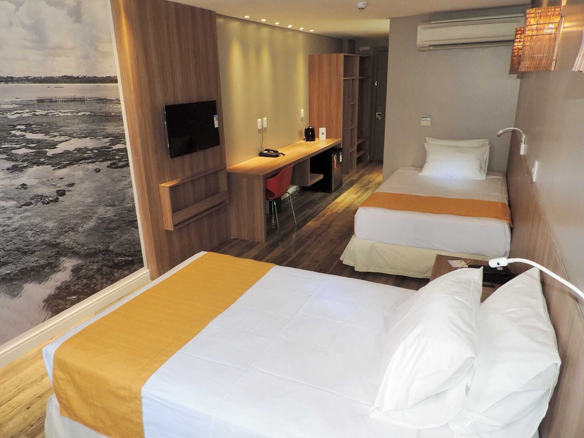A hotel room with two beds, a desk, and a TV.