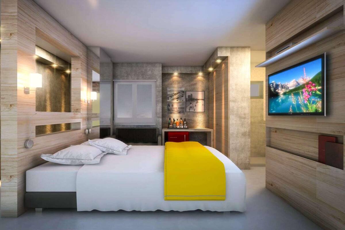 Une chambre d’hôtel moderne avec un grand lit, un téléviseur fixé au mur et un petit espace bureau.