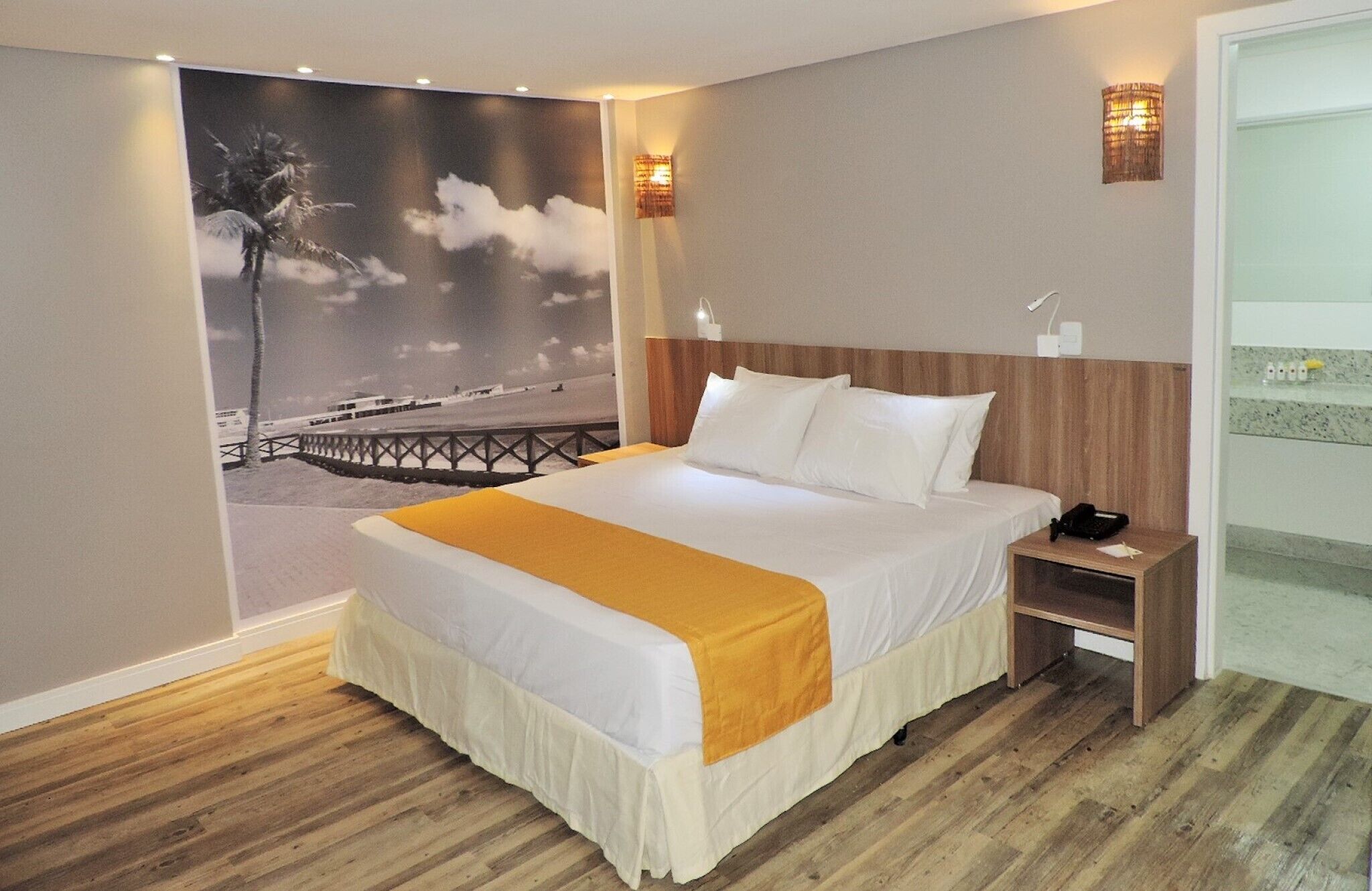 A hotel room with a large bed, a nightstand, a wall-mounted lamp, and a painting of a snowy landscape.