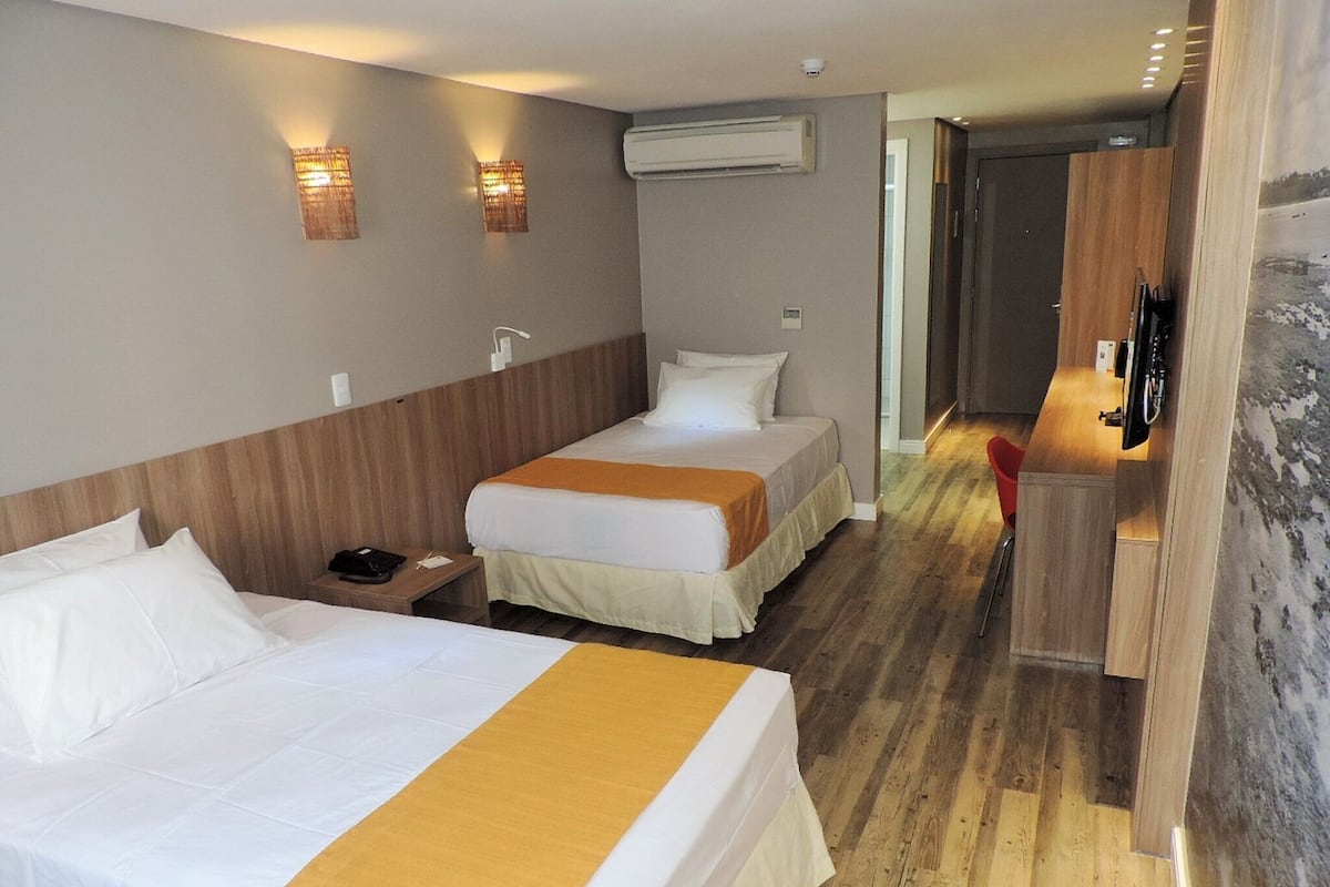 Une chambre d’hôtel avec deux lits, une tête de lit en bois, une table de chevet avec un téléphone et un téléviseur posé sur un meuble en bois.