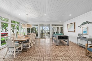 A spacious dining area with a wooden table and chairs, a pool table, and large windows offering views of the outdoors.