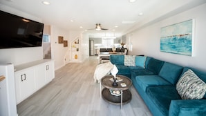Un salon moderne avec un canapé de couleur turquoise, un téléviseur à écran plat et un coin repas à l’arrière-plan.