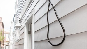 Une pomme de douche fixée au mur, dotée d’un flexible, une poignée de porte et une fenêtre avec des stores.
