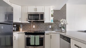 Une cuisine moderne avec des meubles blancs, un réfrigérateur en acier inoxydable, un four à micro-ondes, une cuisinière et un lave-vaisselle.