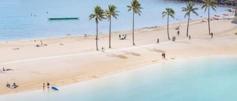 A beach with clear blue water, palm trees, and a sandy shore.