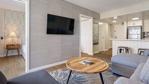 Un salon moderne avec un canapé gris, une table basse ronde en bois et un téléviseur à écran plat fixé au mur.