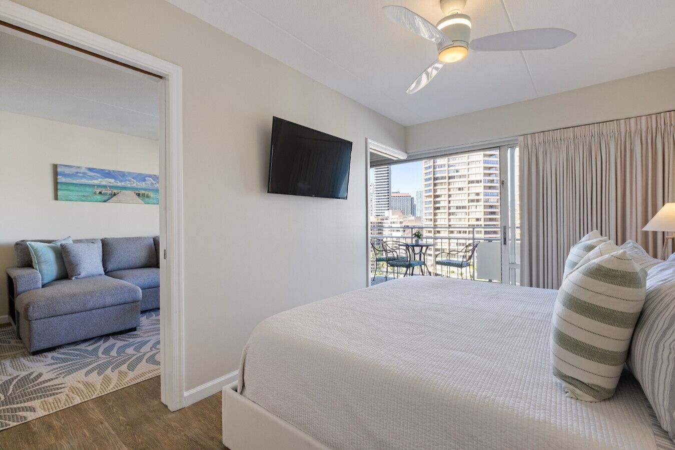 A hotel room with a bed, a sofa, a TV, and a balcony with a view of buildings.