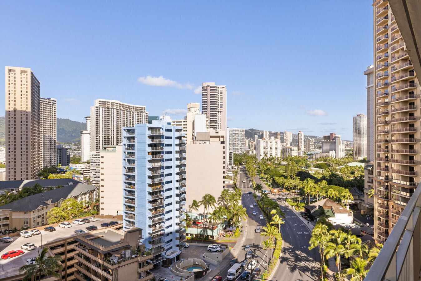 Un edificio alto con múltiples balcones, rodeado de palmeras y otros edificios.