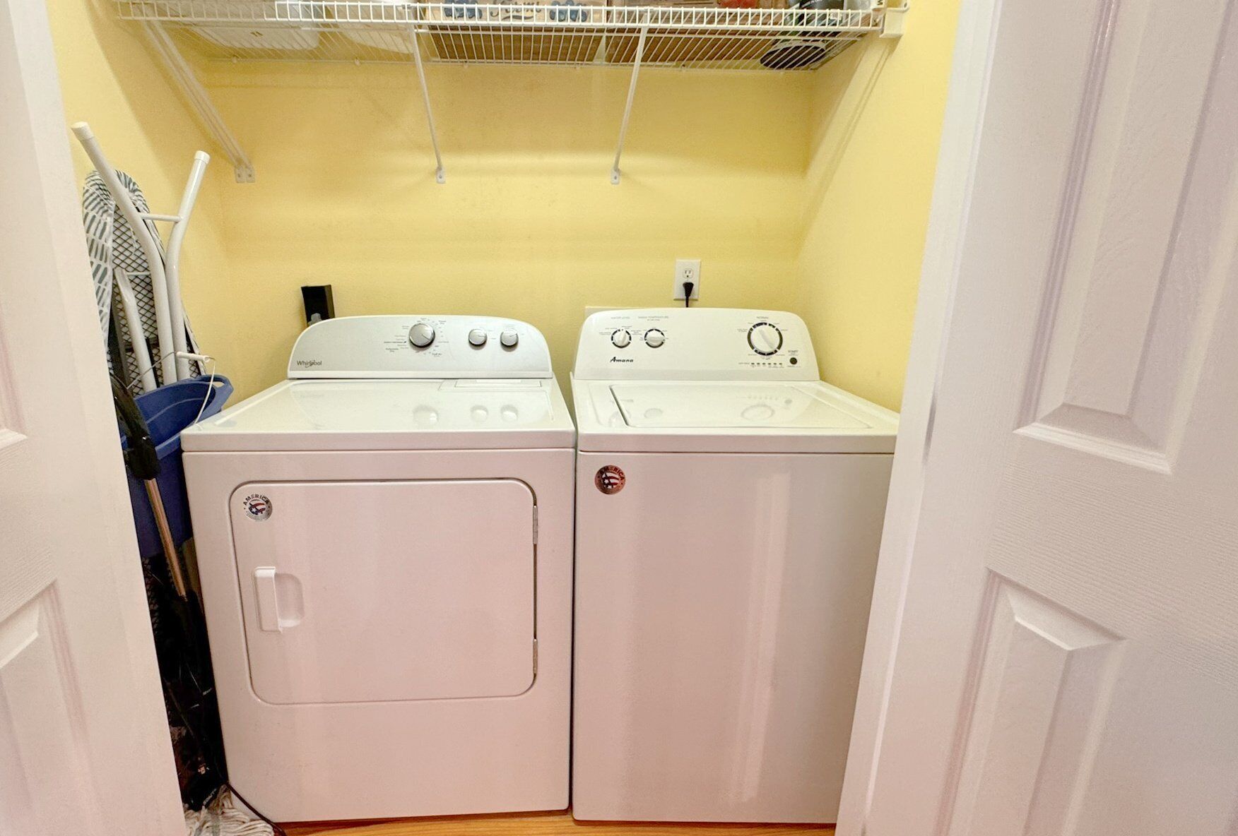 A laundry room with two stacked washers and dryers, a drying rack above, and a power outlet on the wall.
