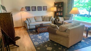 Una sala de estar con sofá, sillones, una mesa de centro, una estantería y una ventana con vistas al exterior.