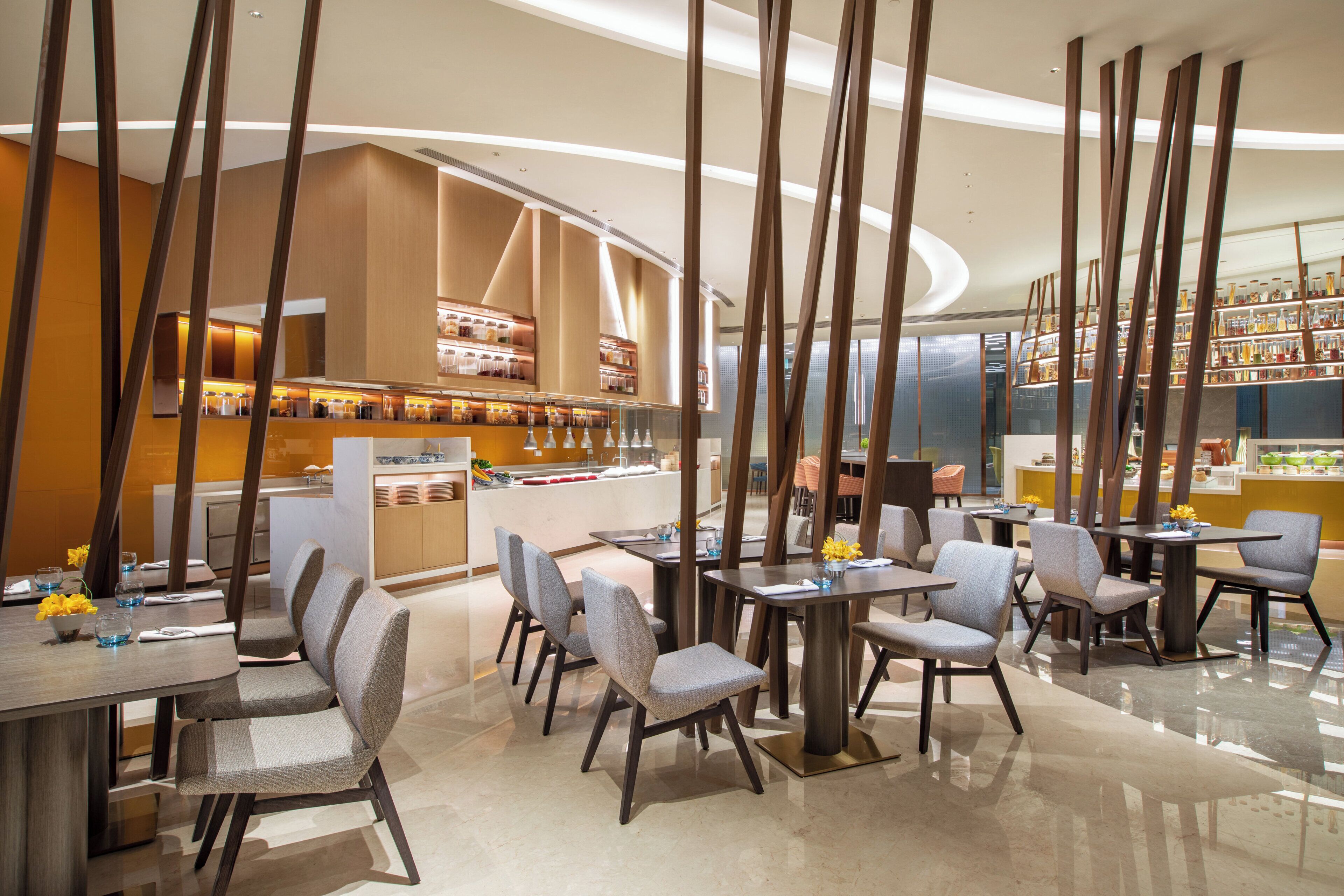 A modern restaurant interior with high ceilings, wooden beams, and a central bar area.