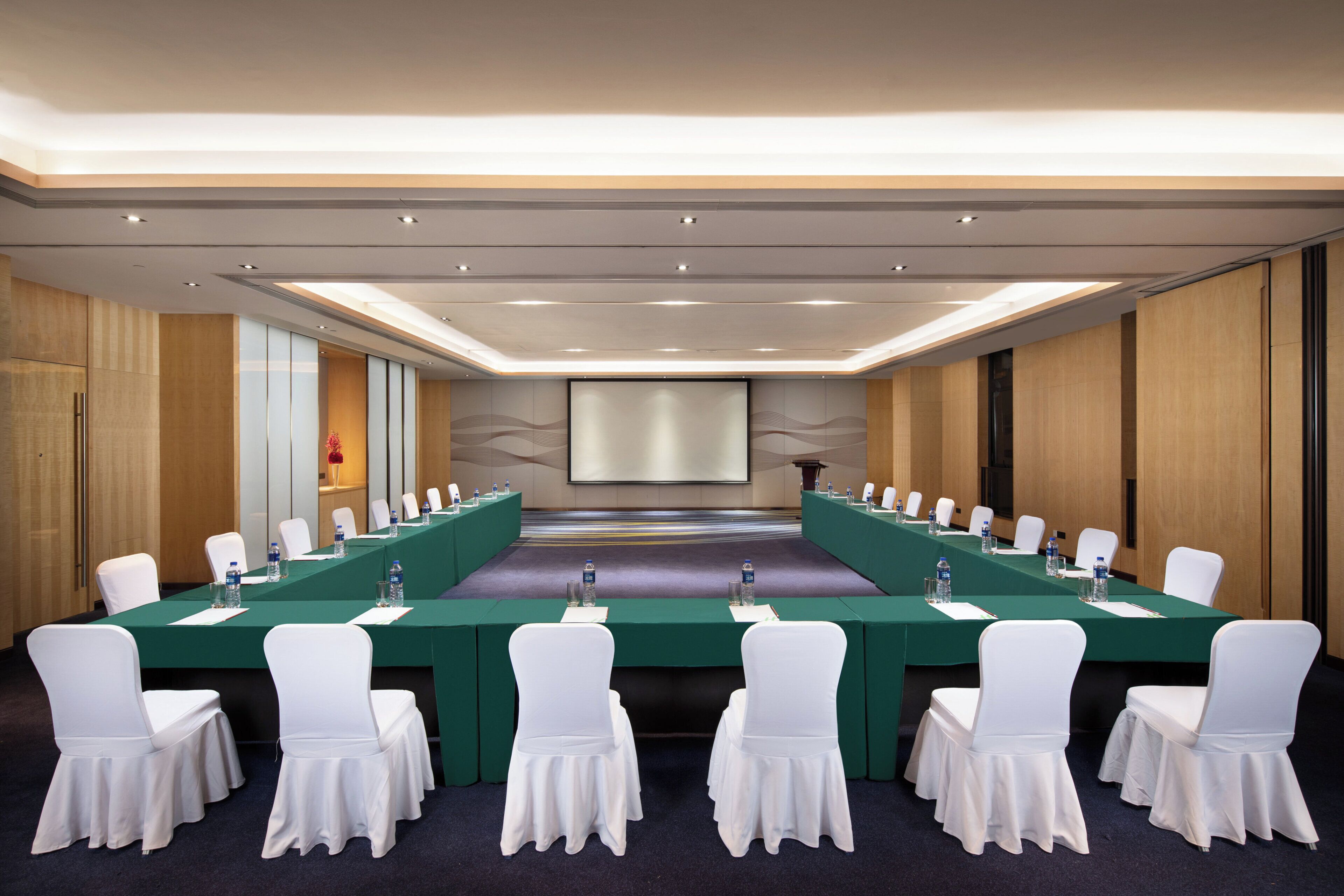 Une salle de conférence avec une longue table, des chaises blanches et un écran de projection.