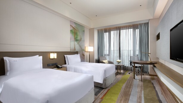 A hotel room with two beds, a desk, a chair, a TV, and a window with curtains. - Holiday Inn Shunde by IHG (Foshan)