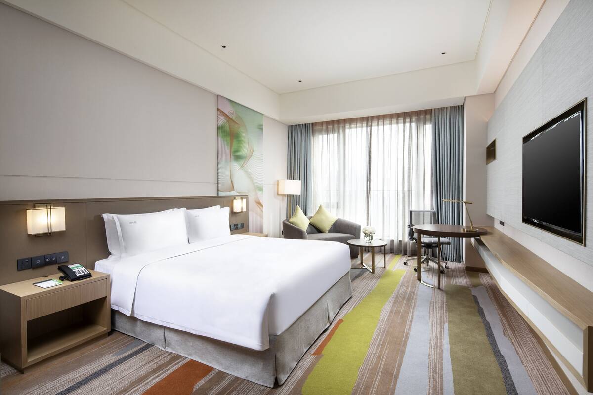 A hotel room with a large bed, a desk, a chair, a TV, and a window with curtains.