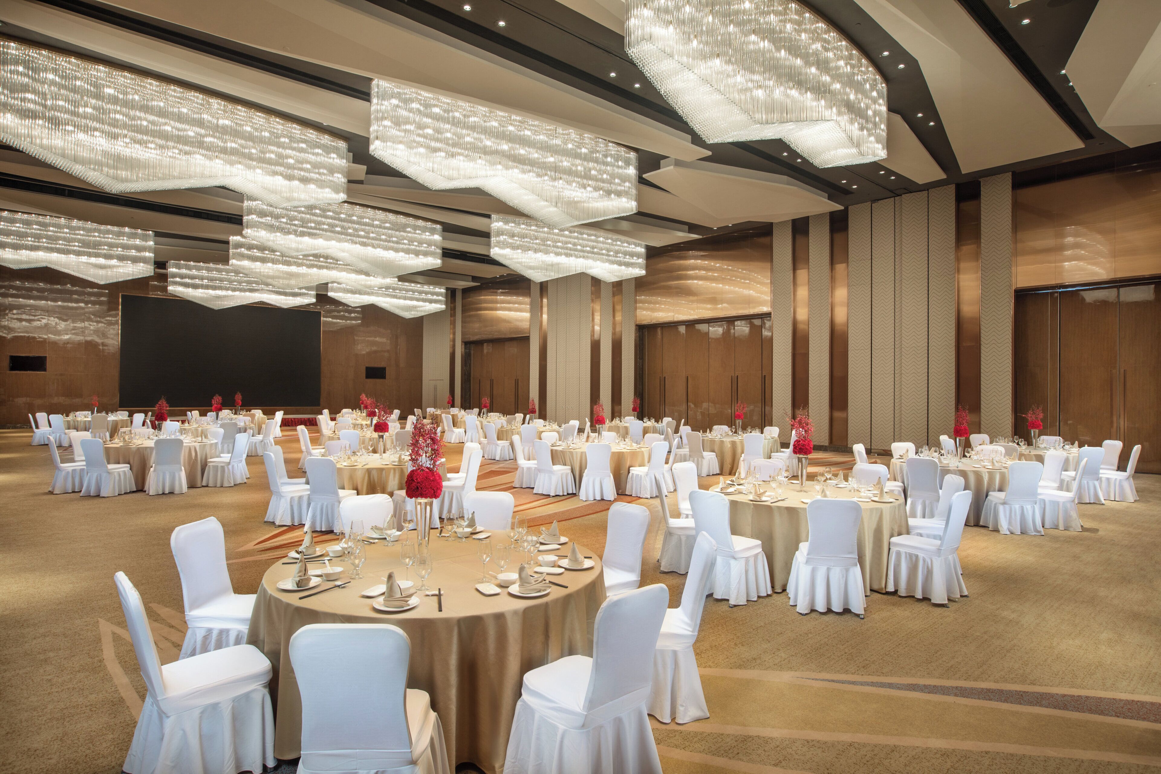 Un salón de banquetes con mesas redondas, sillas blancas y candelabros.