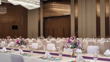 Une salle de banquet où les tables sont dressées pour un événement formel, avec des compositions florales en guise de centre de table et des nappes blanches.