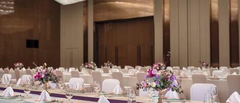 A banquet hall with tables set for a formal event, featuring floral centerpieces and white tablecloths.