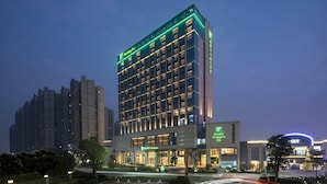 A Holiday Inn hotel with a modern design, featuring a prominent green sign at the top, multiple floors, and a well-lit entrance. - Holiday Inn Shunde by IHG (Foshan)