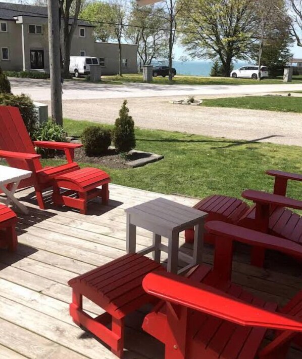 A deck with red Adirondack chairs and a small table, overlooking a residential area with houses and a body of water.