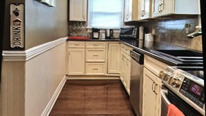 A narrow kitchen with wooden flooring, white cabinetry, a microwave, a stove, and a fish hanging from the ceiling.