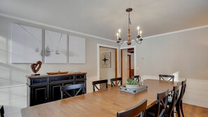 Un coin repas avec une table en bois, des chaises noires, un lustre et un espace cuisine doté de placards et d’une décoration en forme de cœur.