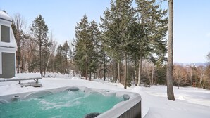 Un bain à remous entouré de terre et d’arbres couverts de neige, avec un bâtiment en arrière-plan.