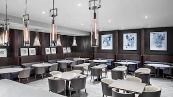 Un restaurante moderno con mesas redondas y sillas acolchadas, lámparas colgantes y arte abstracto en las paredes.